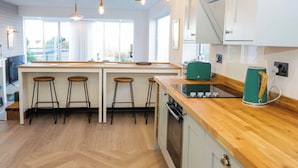 A modern kitchen with a central island, bar stools, a green kettle, and a wooden countertop. - Awel Y Mor (Prestatyn)