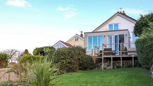 A modern two-story house with a large front yard, a wooden deck, and a stone wall. - Awel Y Mor (Prestatyn)