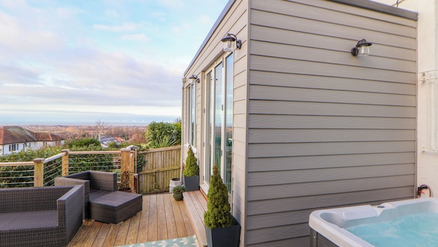 A deck with outdoor furniture, a hot tub, and a view of the city. - Awel Y Mor (Prestatyn)