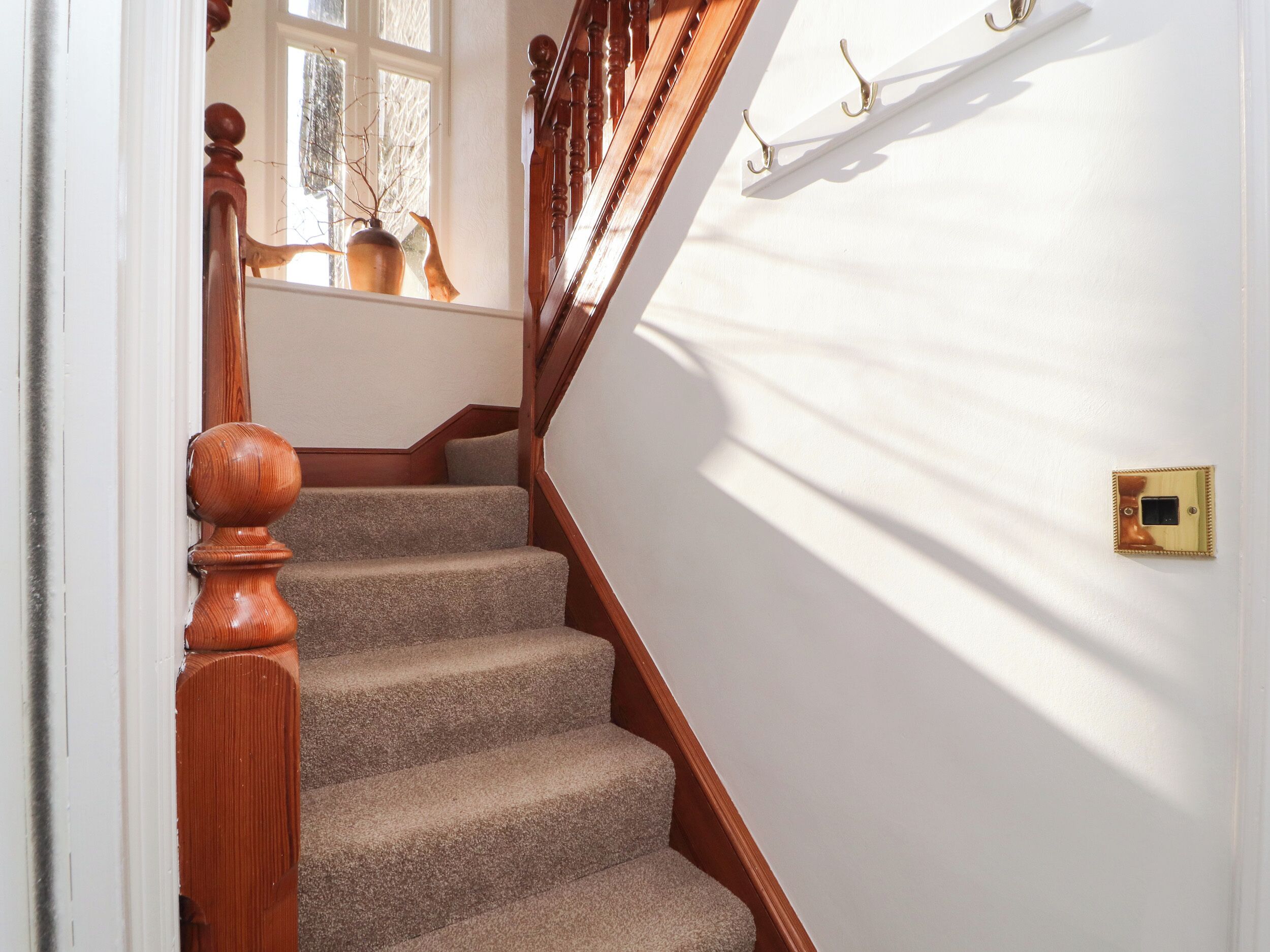 A staircase with wooden balusters and a handrail, carpeted steps, and a wall-mounted light switch.