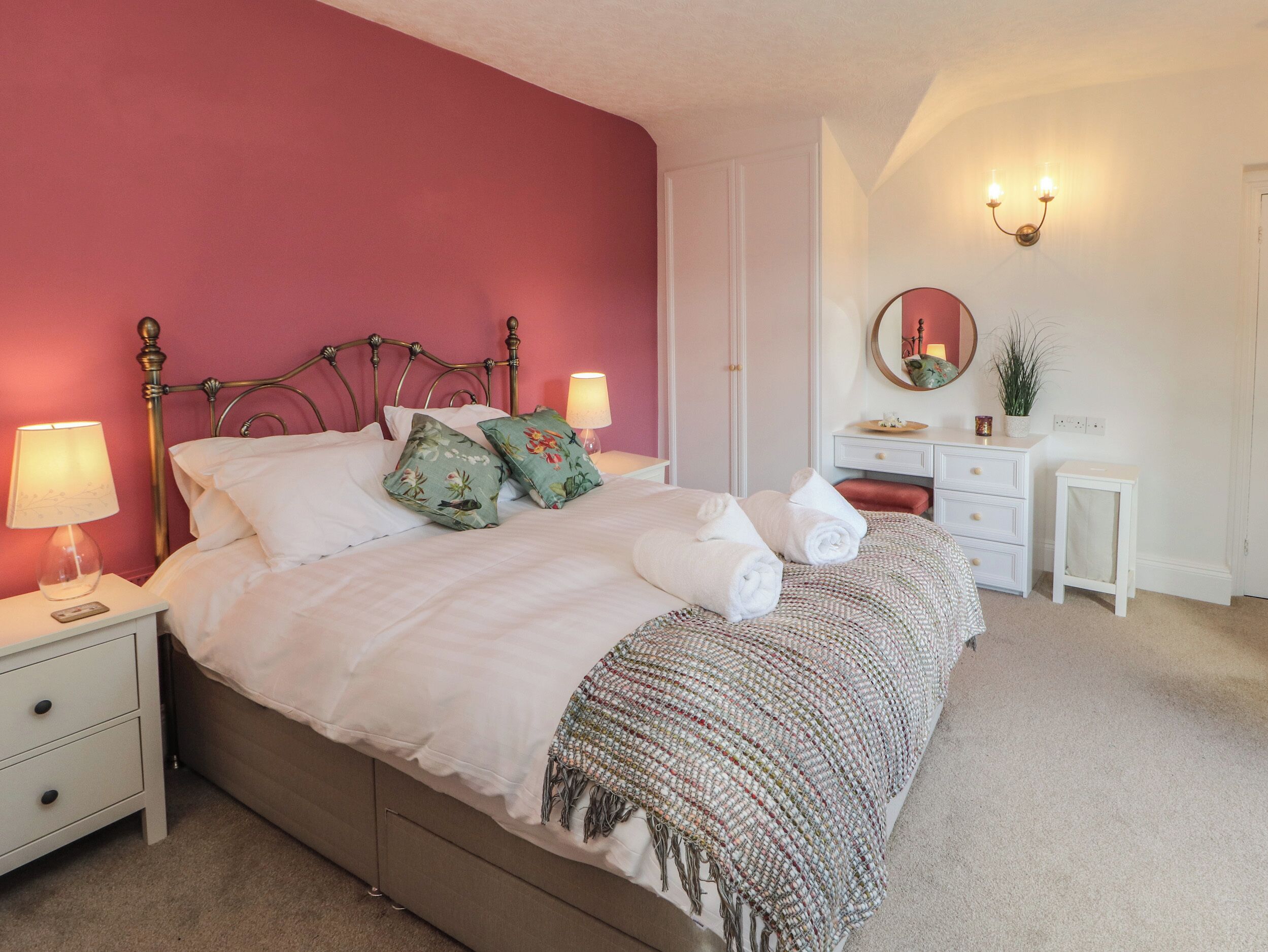 A bedroom with a bed, bedside tables, a nightstand, a dresser, a mirror, and a wall sconce.