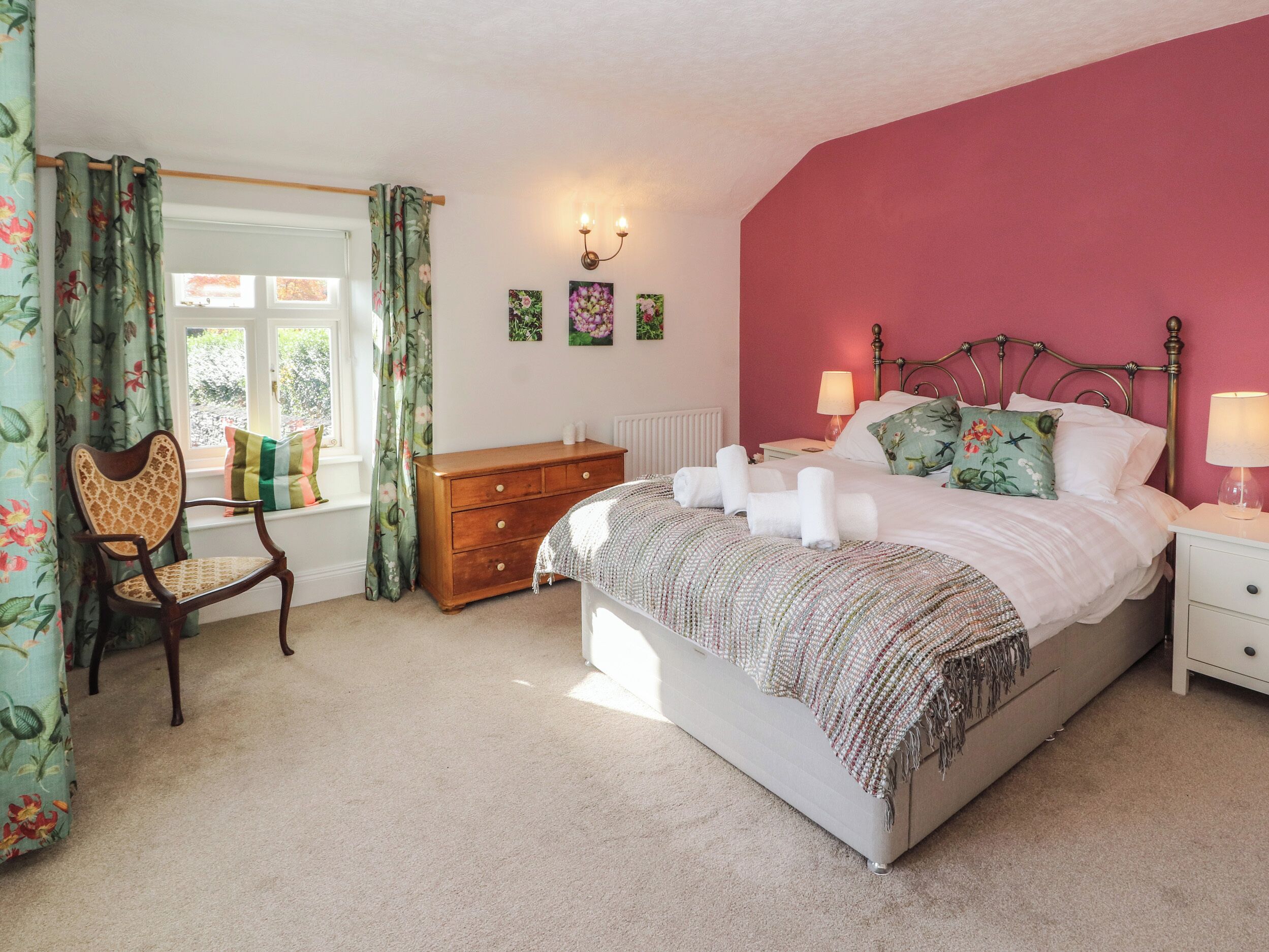 A bedroom with a bed, a dresser, a chair, a window with curtains, and wall art.