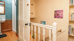 A hallway with a white door, a wooden floor, a sink, and a bookshelf. - Gardeners Cottage (Millom)