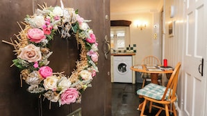A wooden door with a wreath, a kitchen area with a washing machine, and a dining table with chairs. - Gardeners Cottage (Millom)