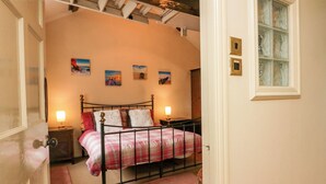 A bedroom with a bed, bedside tables, a window, and artwork on the wall. - Gardeners Cottage (Millom)