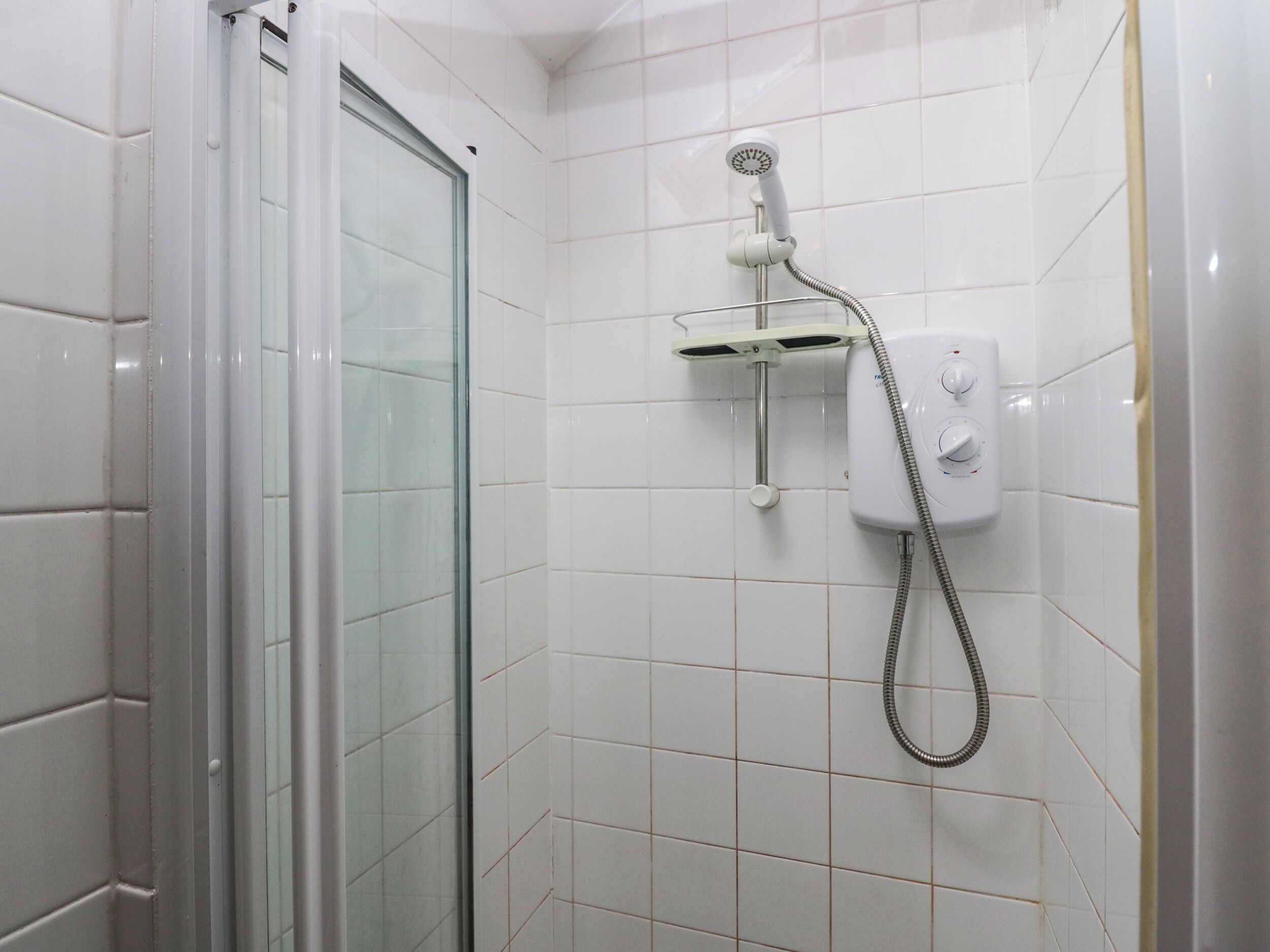 A bathroom with white tiled walls, a glass shower enclosure, and a wall-mounted showerhead with a flexible hose.