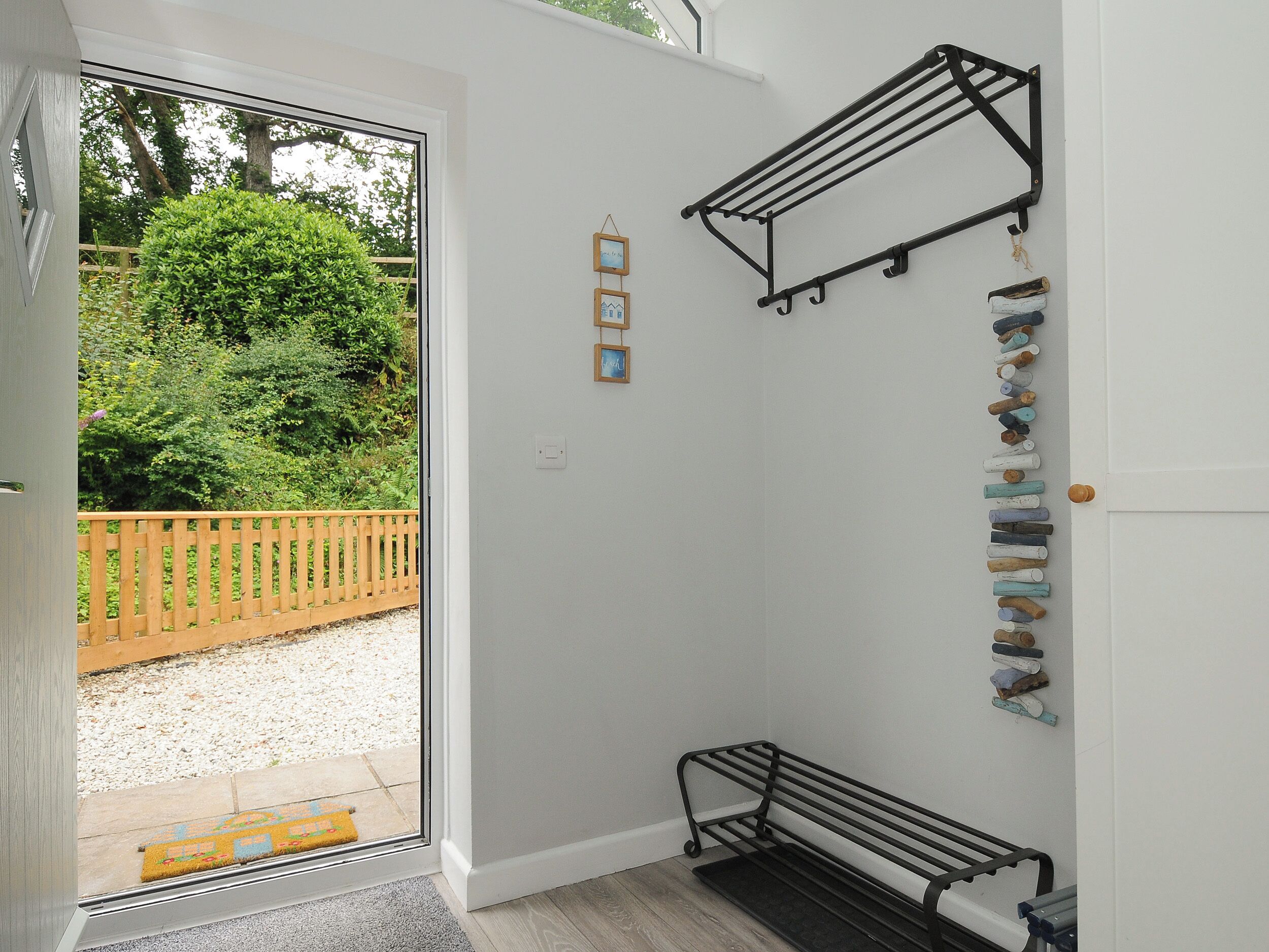 Een kamer met een bankje, een droogrek en een deur naar een tuin.