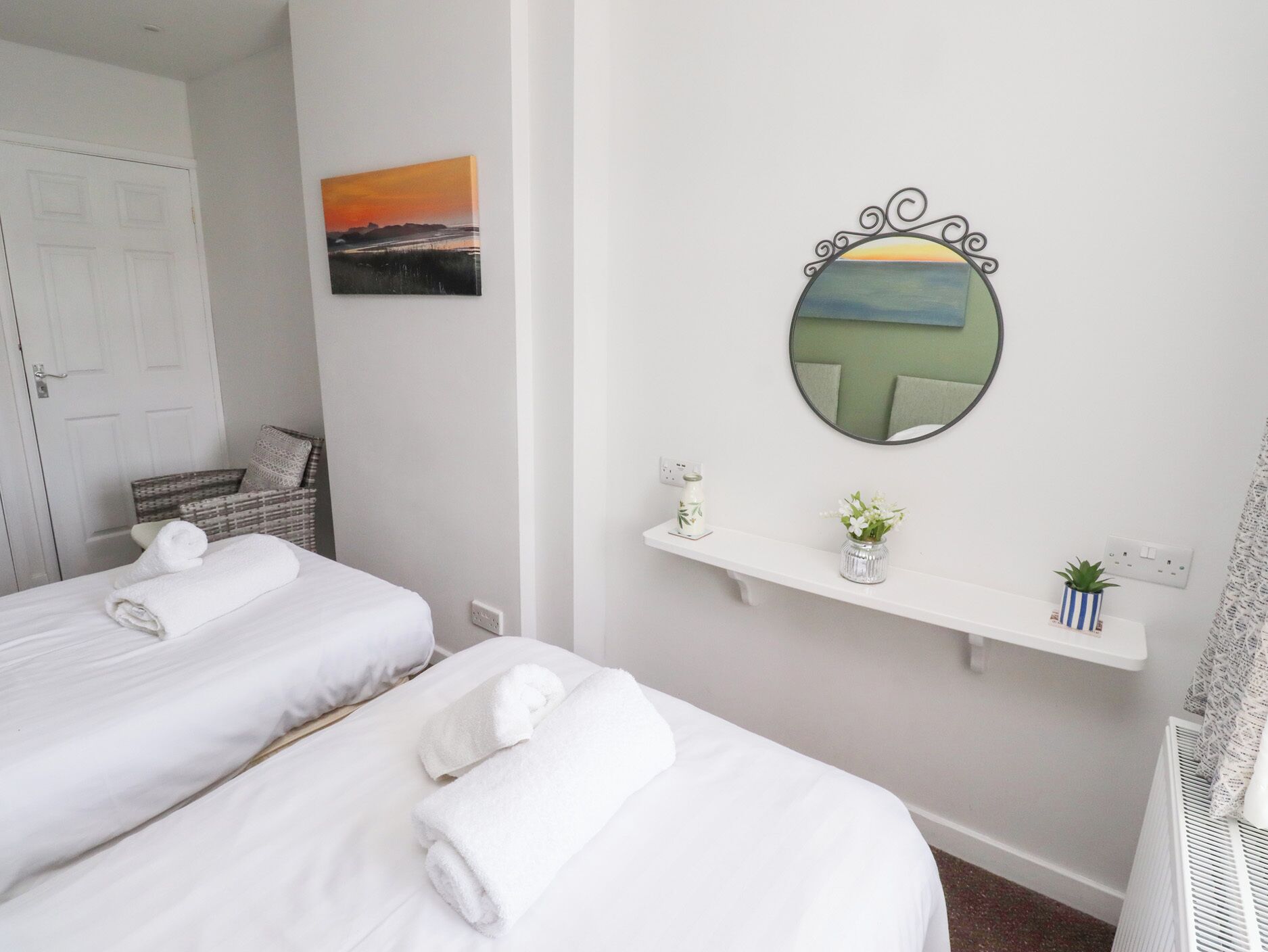 Habitación de hotel con dos camas, un cuadro, un espejo y una estantería con plantas.