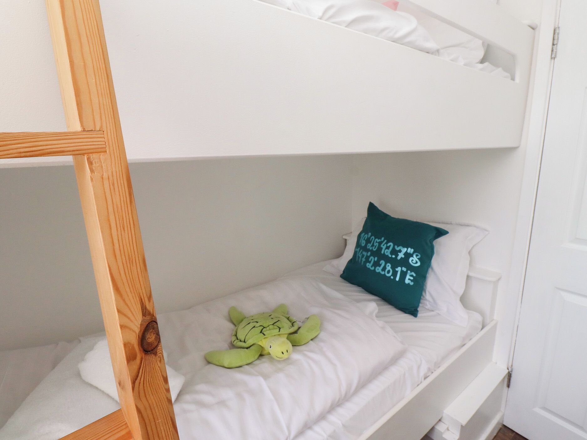 Ein Stockbett mit einem grünen Plüschtier und einem Kissen mit Koordinaten auf einer weißen Matratze.