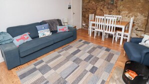 A living room with a blue sofa, white chairs, a wooden table, and a patterned rug.