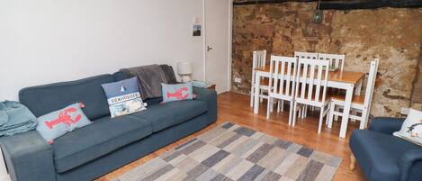 A living room with a blue sofa, white chairs, a wooden table, and a patterned rug.