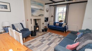 A cozy living room with a sofa, a chair, a table, a fireplace, and a large window.