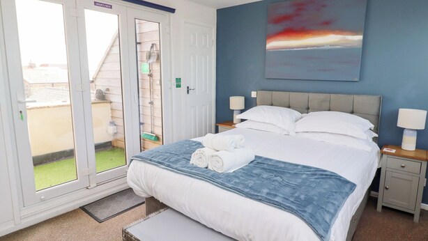 A hotel room with a bed, a painting, a window, and a door.