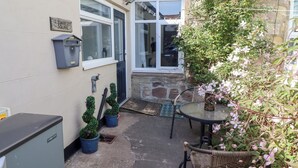 A small courtyard with a door, a window, a table, and potted plants.