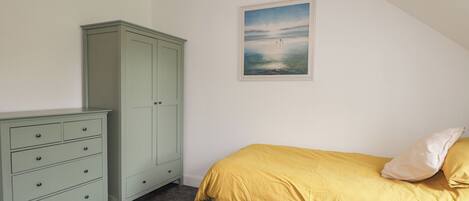 A bedroom with a bed, a green dresser, and a framed picture on the wall.