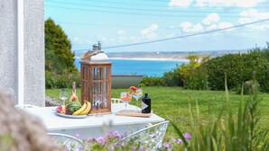 A table set outdoors with a view of the sea, a lantern, and a bottle of wine.