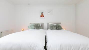 A bedroom with two single beds, white bedding, and two wall-mounted lamps.