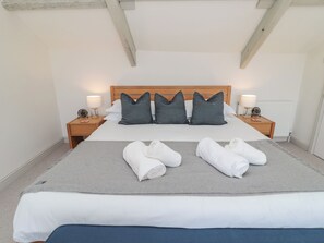 A neatly made bed with a grey blanket, two white towels, and striped pillows. There are two bedside tables with lamps and a wooden headboard. - Eider Cottage (Morpeth)