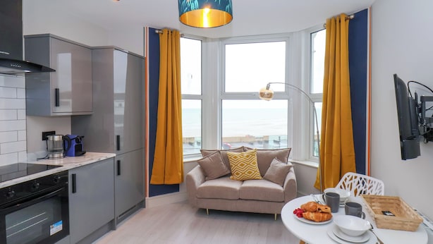 A modern kitchen with a built-in oven, a coffee maker, and a dining area with a table set for breakfast. - Apt 6 @ Hunter's Quay (Bridlington)