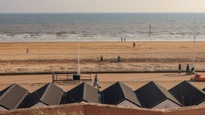 A beach with people walking, a no parking sign, and a row of buildings with sloped roofs. - Apt 6 @ Hunter's Quay (Bridlington)