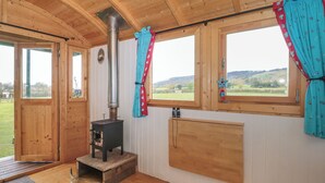 A cozy cabin interior with a wood stove, large windows, and a view of the outdoors. - Harri's Hut (Taunton)