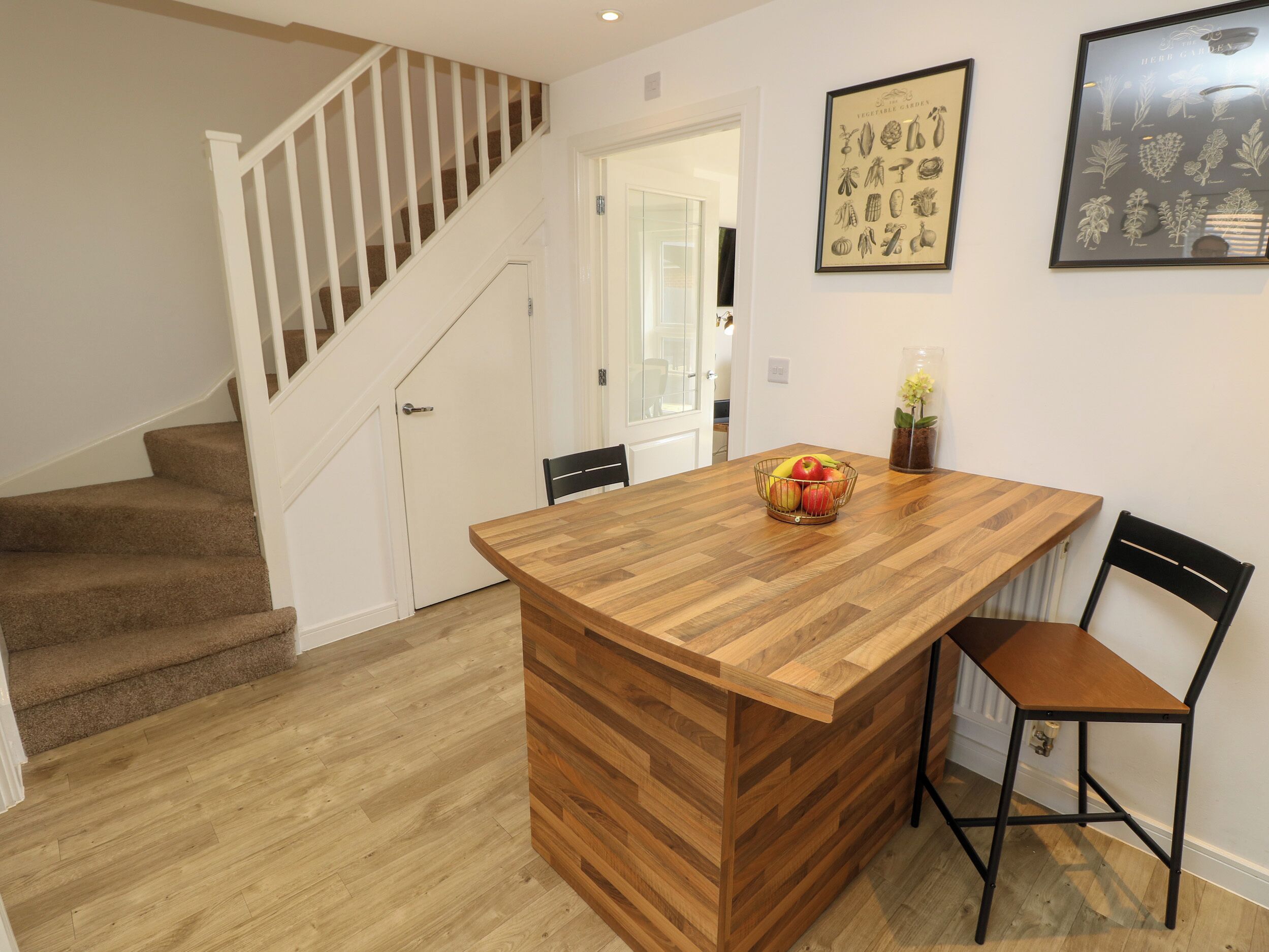 A kitchen with a wooden island, a staircase, and two framed botanical prints on the wall.