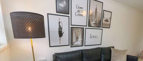 Una sala de estar moderna con un sofá de cuero negro, una lámpara de pie con estampado y varias obras de arte enmarcadas en la pared.