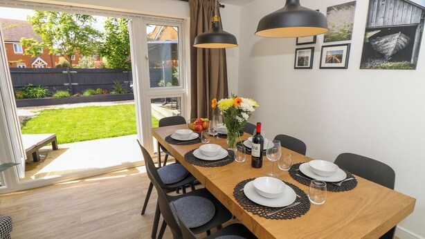 Comedor con mesa de madera dispuesta para seis comensales, sillas y vista a un patio trasero a través de puertas de vidrio.