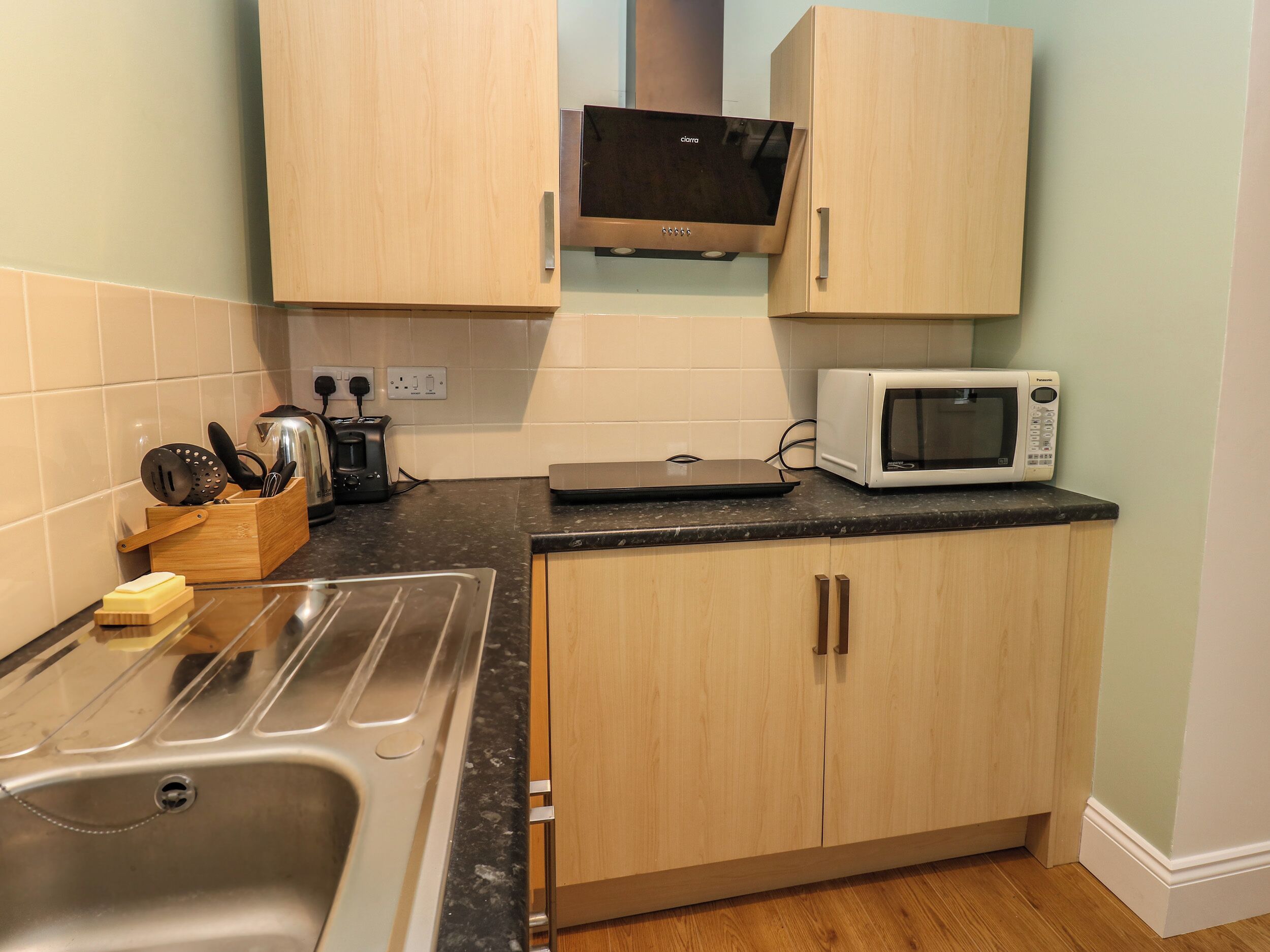 Una cocina con armarios de madera, un lavamanos de acero inoxidable, un microondas y un tostador.