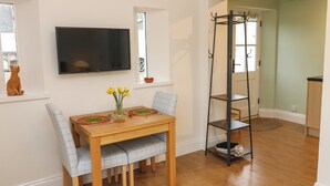 A dining area with a wooden table, chairs, a vase with flowers, a television on the wall, and a black shelf unit. - Woodland View (Bishop Auckland)