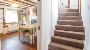 A staircase with carpeted steps leading to a dining area with a table and chairs. - Brook Cottage (Saxmundham)