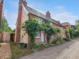 A traditional brick house with a white door and windows, surrounded by greenery and a gravel driveway.