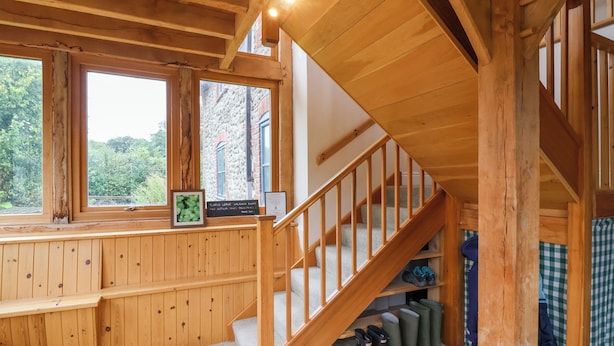 Interior de madera con una escalera, un ventanal con vistas a árboles y un estante con botas.