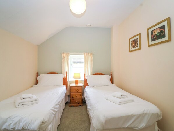 Habitación doble con dos camas individuales, un aparador de madera, una mesita de noche con lámpara y un ventanal con cortinas.