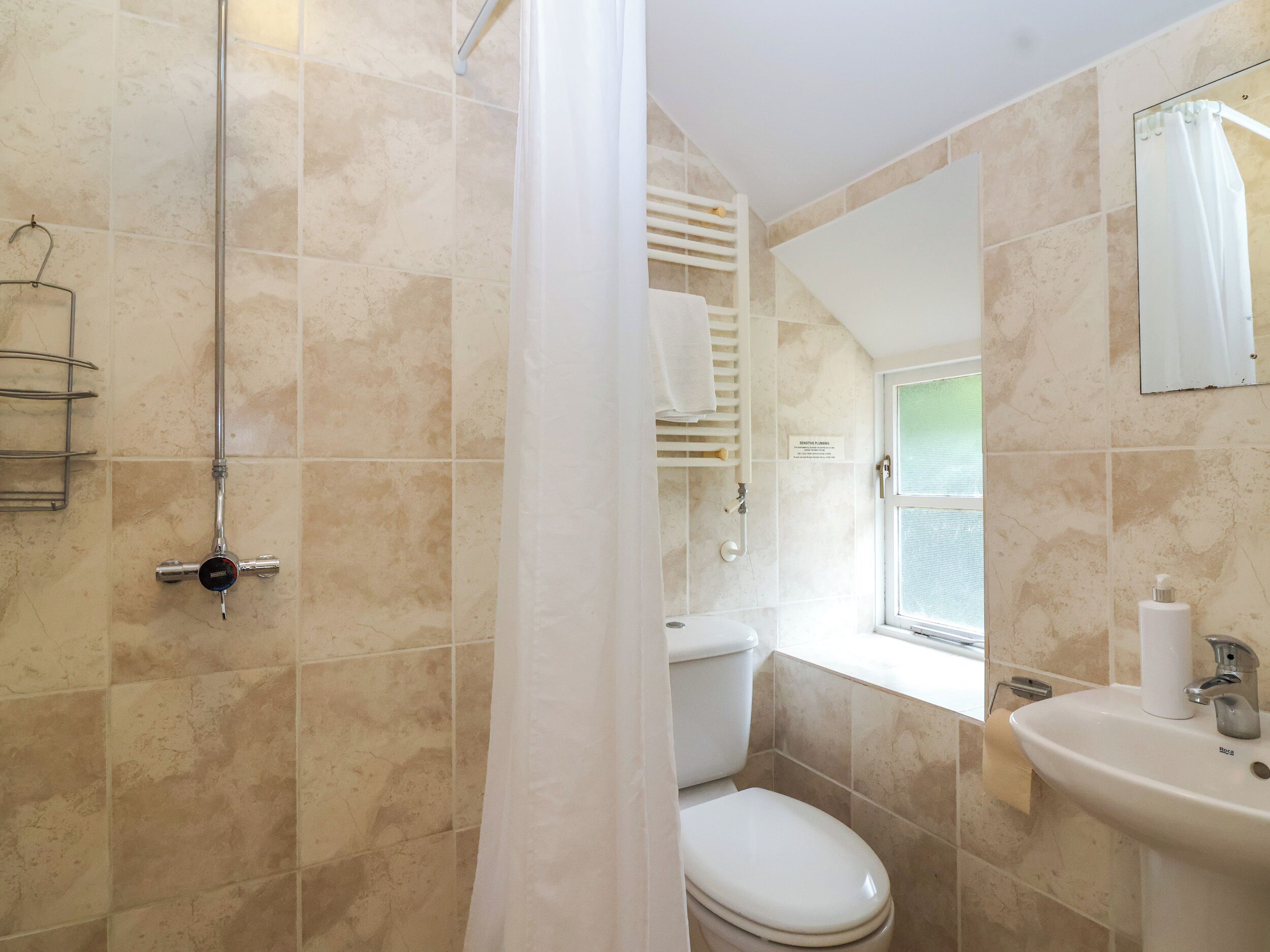 A bathroom with beige tiles, a shower with a glass door, a toilet, a sink with a mirror, and a towel rack.