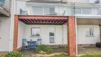A two-story house with a covered patio area featuring a table and chairs, a small garden, and a satellite dish.