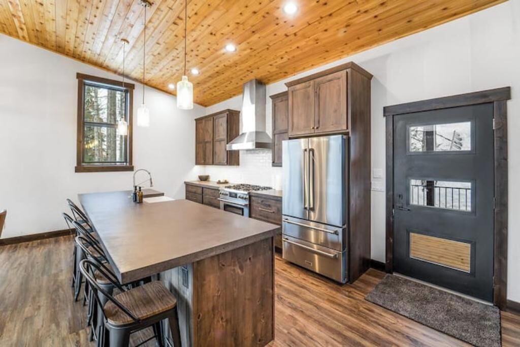 A modern kitchen with a wooden ceiling, stainless steel appliances, and a large island with bar stools.