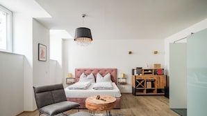 A modern bedroom with a large bed, a grey armchair, a small round table, and a hanging light fixture. - Vienne Prime Apartments (Vienna)