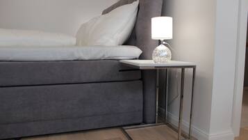 A modern bedroom with a grey sofa bed, a bedside table with a lamp, and a wooden floor.