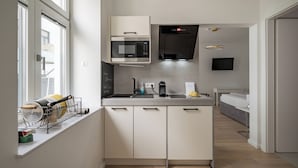 A modern kitchen with a built-in microwave, oven, and gas stove. There is a window with a view of the city, a sink, and a countertop with a coffee maker and a kettle. - Vienne Prime Apartments (Vienna)