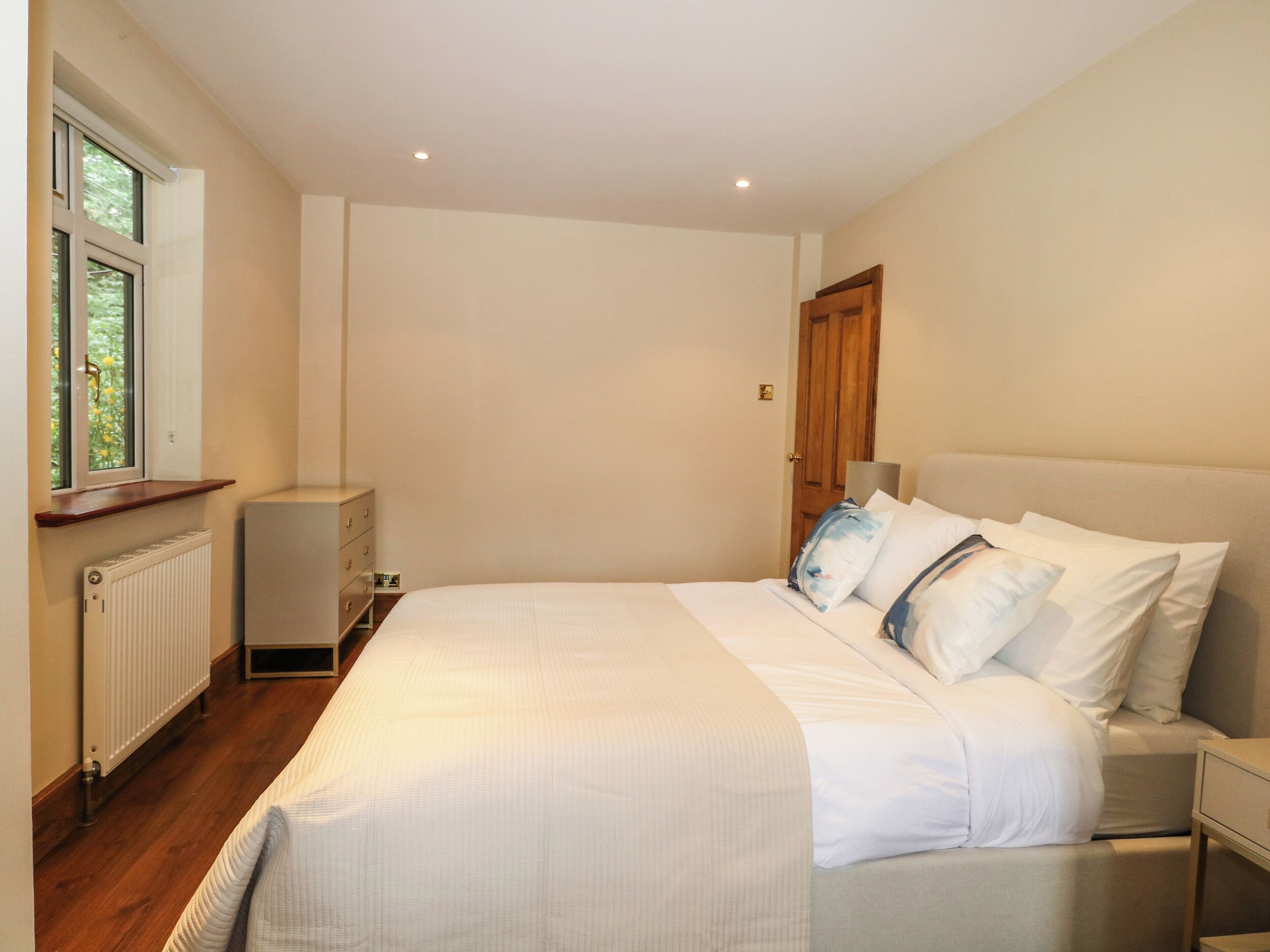 Une chambre à coucher avec un grand lit, une table de chevet, une commode, une fenêtre et un radiateur.