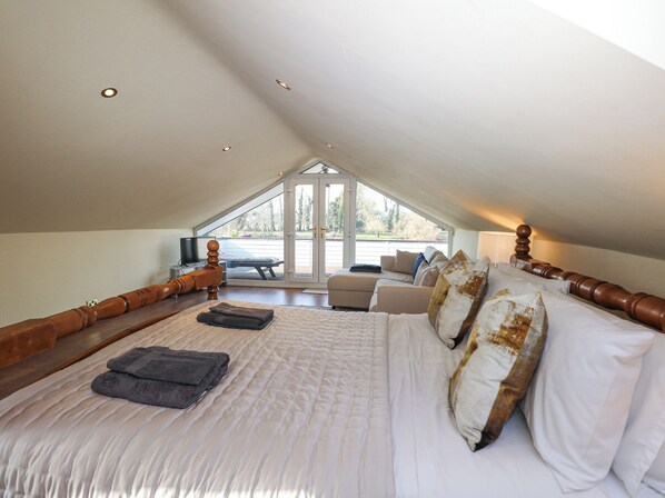 A bedroom with a large bed, a wooden headboard, a television, and a view of the outdoors through a large window.