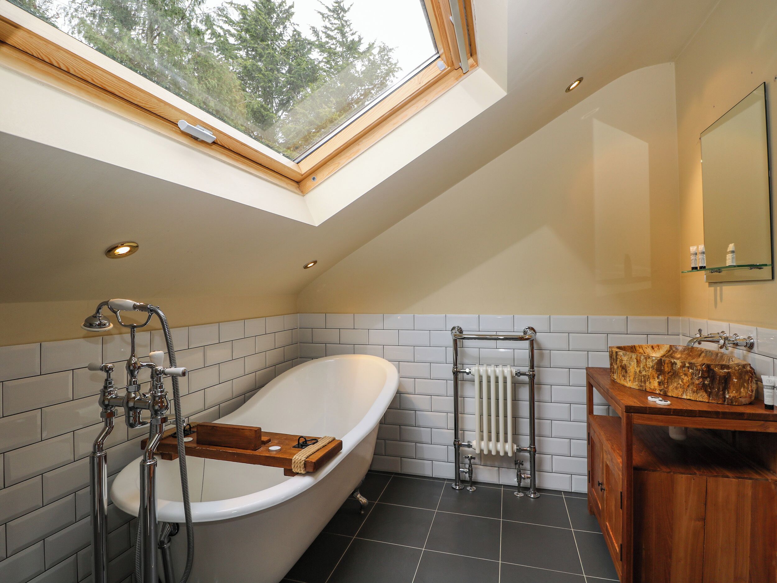 A modern bathroom with a freestanding bathtub, a wooden vanity, a glass shower enclosure, and a skylight.