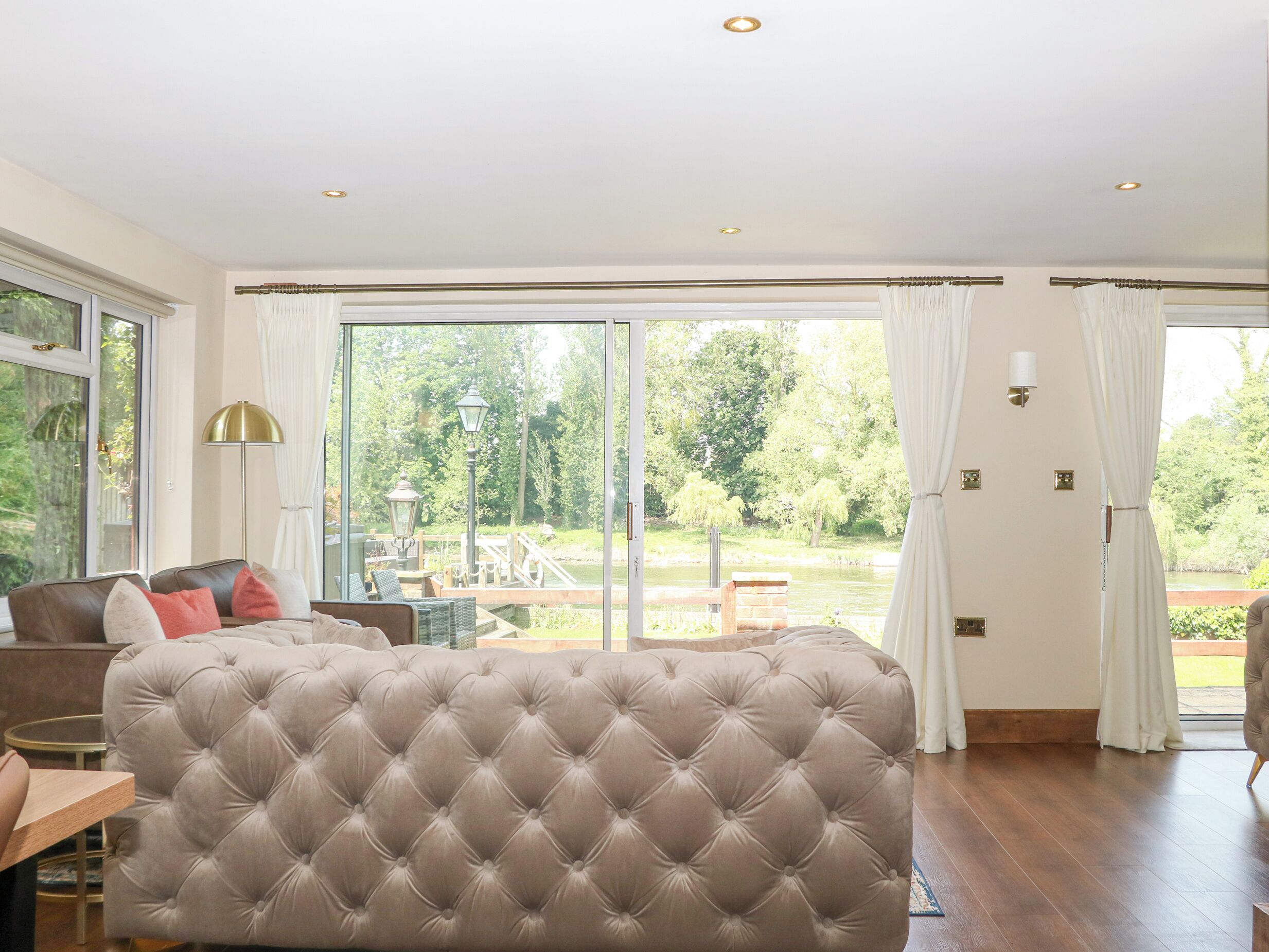 A spacious room with a large tufted sofa, a dining table, and a view of a garden and water feature through large glass doors.