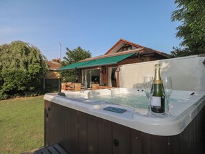 A hot tub with a bottle of champagne and two glasses, a patio with outdoor furniture, and a house in the background. - Coventina (Staines)