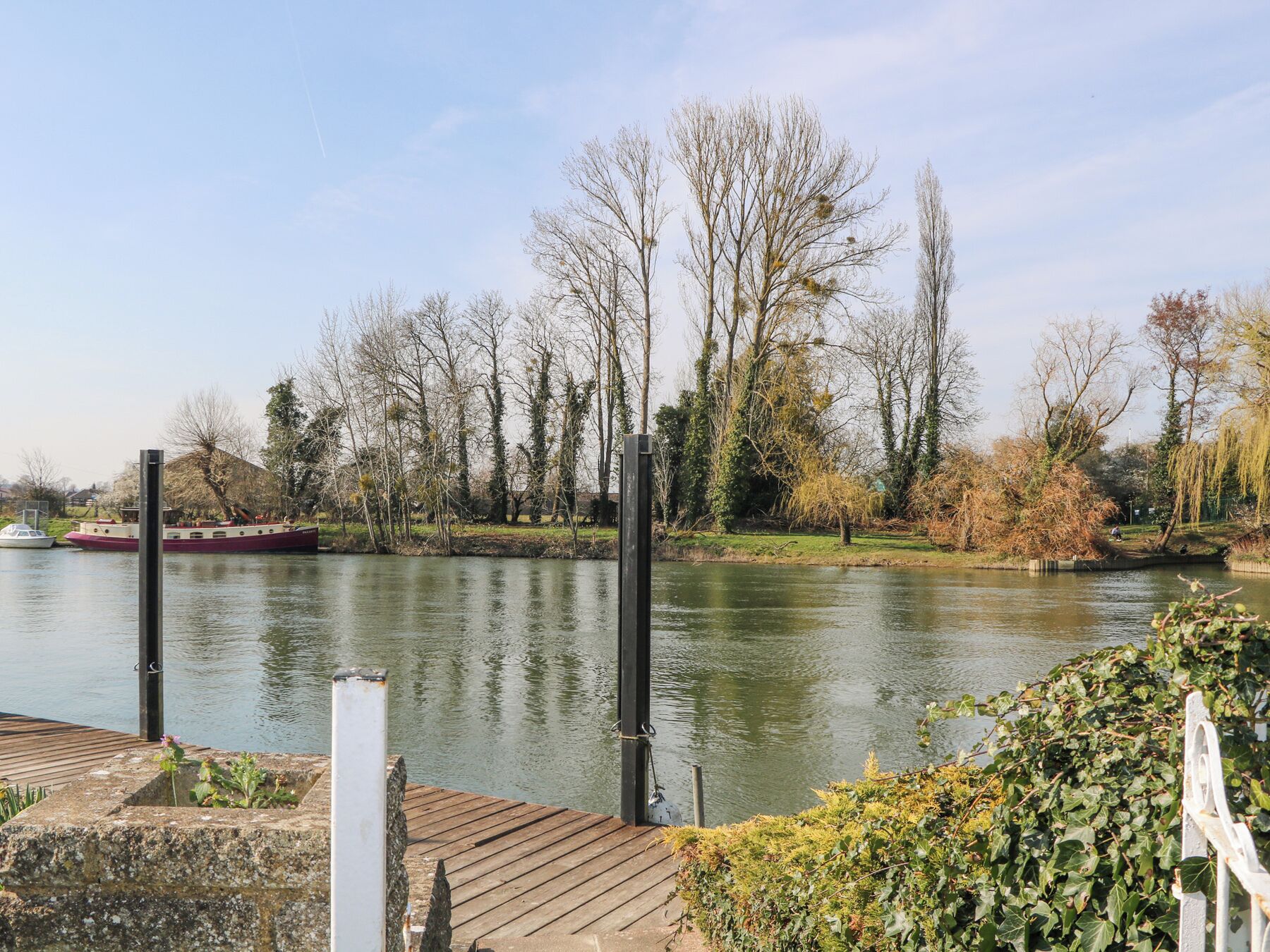 A riverside dock with a wooden platform, a boat moored nearby, and trees lining the riverbank.
