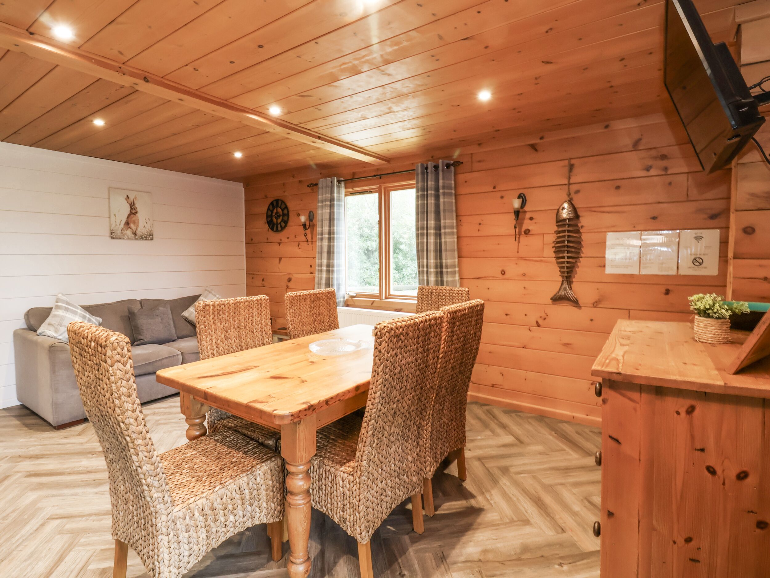 Interior de una cabaña de madera con una mesa de comedor y sillas, un sofá y una decoración de pez en la pared.