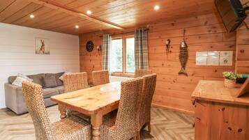 Interior de una cabaña de madera con una mesa de comedor y sillas, un sofá y una decoración de pez en la pared.