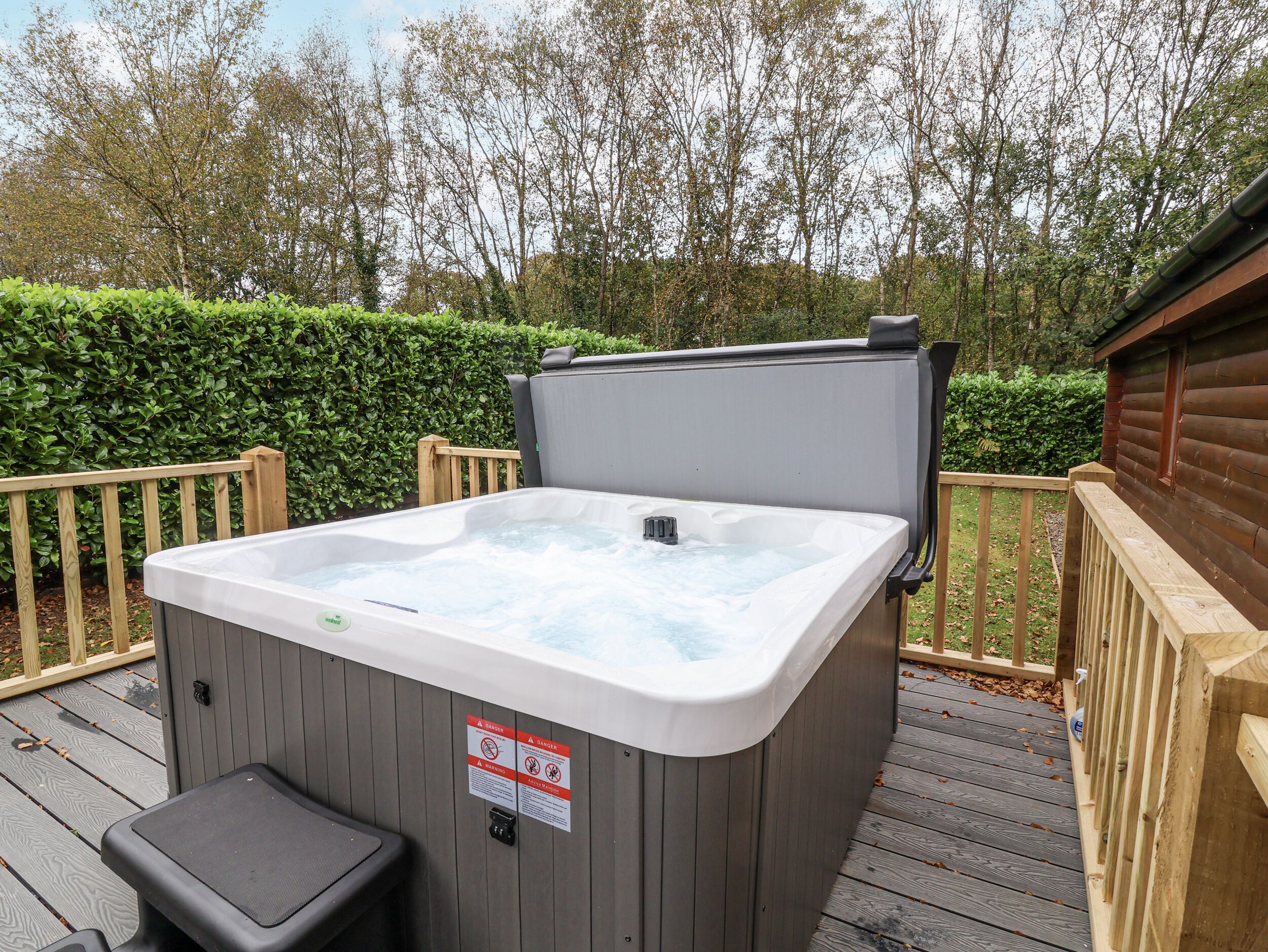 Ein Whirlpool auf einer Terrass mit Holzgeländer und ein Holzhäuschen im Hintergrund.