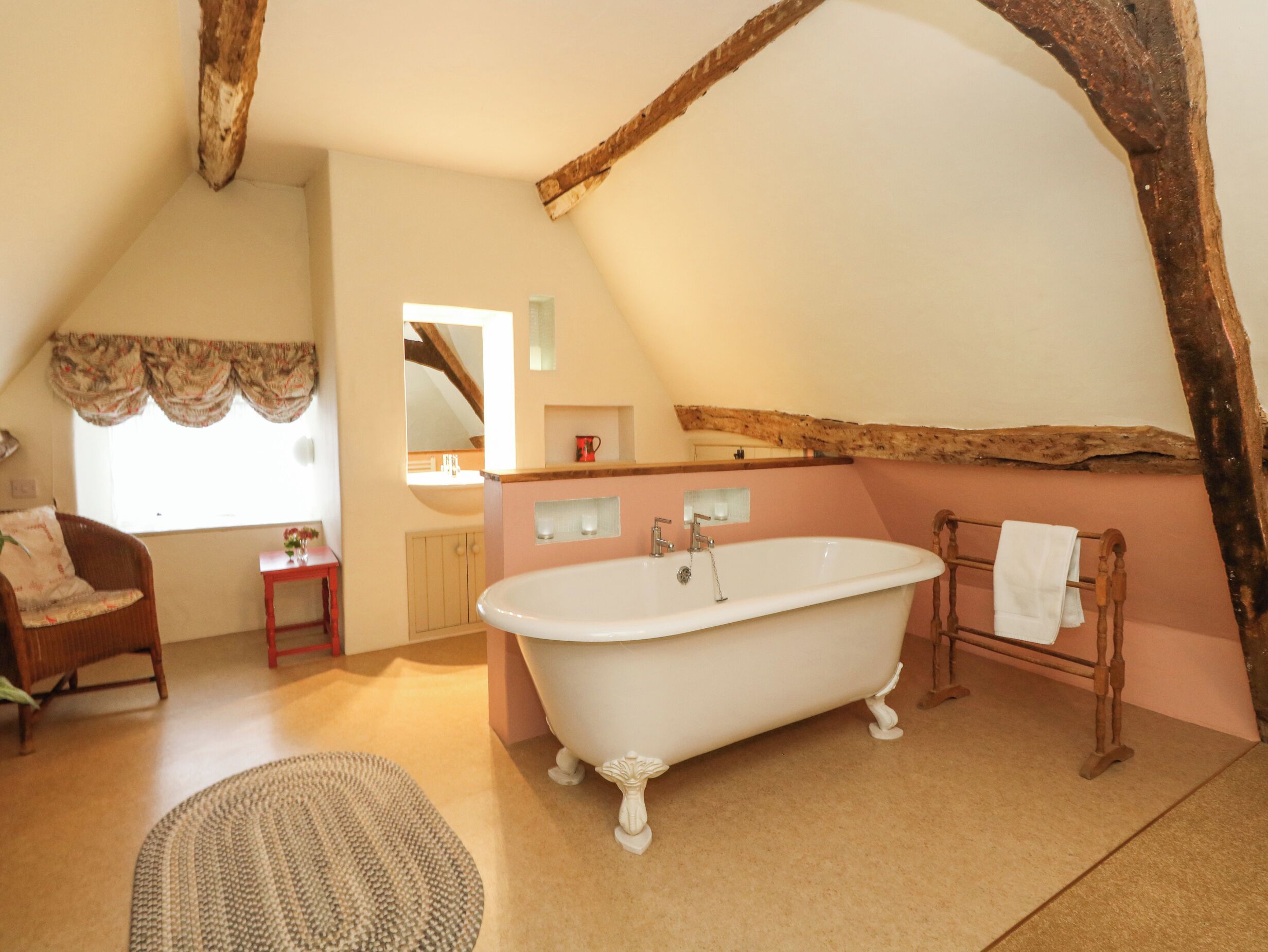 A bathroom with a freestanding bathtub, a wooden chair, a small table, and a mirror.